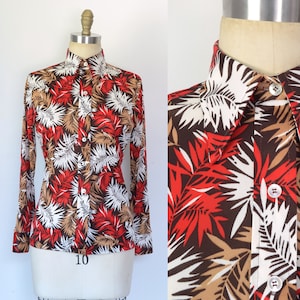May include: A long-sleeved button-down shirt with a brown, white, and red tropical leaf print. The shirt has a pointed collar and a button-up front.