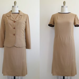 May include: A two-piece suit in a light brown colour. The jacket has a notched collar, long sleeves, and a button fastening. The skirt is knee-length and has a straight silhouette.