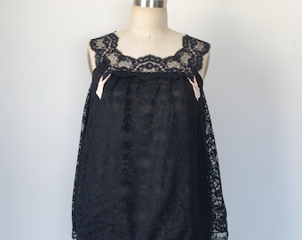 Puede incluir: Una blusa de encaje negro con escote festoneado y detalles de cinta rosa. La blusa es sin mangas y tiene un corte holgado.