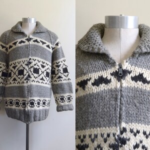 May include: A gray, black, and white patterned knitted cardigan with a zipper closure. The cardigan has a thick collar and a geometric pattern.