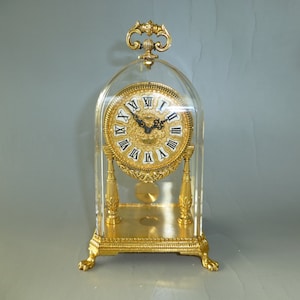 May include: A gold-toned mantle clock with a clear glass dome and Roman numeral face.