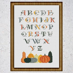 May include: Cross stitch pattern featuring the alphabet in a black and white font with orange and yellow accents. The letters are surrounded by a decorative border. The bottom of the pattern features a row of pumpkins and gourds in various colors.