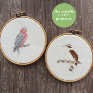 May include: Two embroidery hoops with cross-stitch designs of Australian birds. The left hoop features a pink and grey galah, while the right hoop features a brown and white kookaburra.