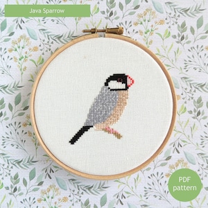 Peut inclure: Broderie au point de croix d'un moineau de Java dans un cercle en bois. L'oiseau présente des détails en point de croix gris, noir et beige, avec un bec rouge et une tête noire. Le texte "Java Sparrow" est au-dessus et "PDF pattern" en dessous.