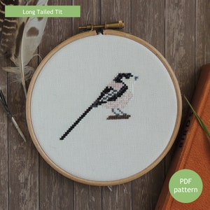 Op de afbeelding: Een kruissteekpatroon van een langstaartmees in een houten borduurring. De vogel is wit met zwarte markeringen en een roze borst. De tekst "Long Tailed Tit" staat bovenaan de afbeelding. De tekst "PDF pattern" staat onderaan de afbeelding.