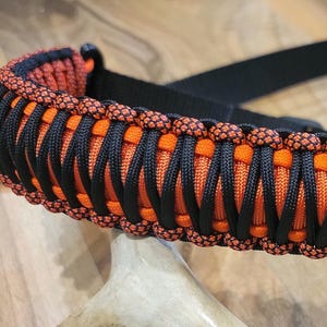 May include: A black and orange paracord strap with a black nylon strap and metal clips. The strap is made with black and orange woven paracord. The text in the image reads: COLOR #1: FLO ORANGE, COLOR #2: BURNT ORANGE, COLOR #3: NEON ORANGE DIAMONDS, COLOR #4: BLACK.