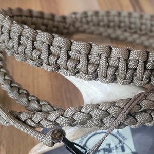 May include: Coyote brown paracord dog collar and leash set. The collar is a wide, woven design, and the leash is a matching braided style. A black metal clip and ring are attached. The text "COLORS #1-4: COYOTE BROWN" is visible.