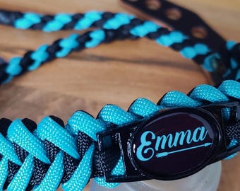 May include: A neon turquoise and black braided dog collar with the name "Emma" on a black oval. The collar has a leather buckle and the text "Bling it customs" on a card.