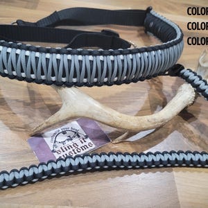 May include: A black, white, and grey paracord sling with metal fixings. The sling is shown with a deer antler and a tag that reads "Bling it Customs". The colour scheme includes white, black, and grey.
