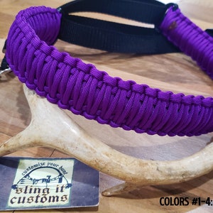 May include: Purple paracord sling with a black strap and a silver hook. The sling is made with a braided pattern and is labeled "sling it customs". The text "COLORS #1-4: ACID PURPLE" is visible at the bottom of the image.