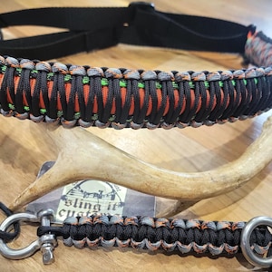 May include: A black and orange paracord dog collar and lead. The collar and lead are made of woven nylon cord and feature metal hardware. The image also includes a deer antler.