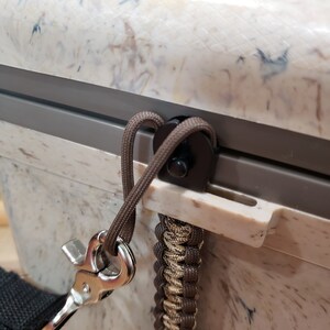 May include: Close-up of a cooler with a speckled white and brown exterior. A brown rope is attached to the cooler with a metal clasp and a braided strap. The cooler has a grey trim.