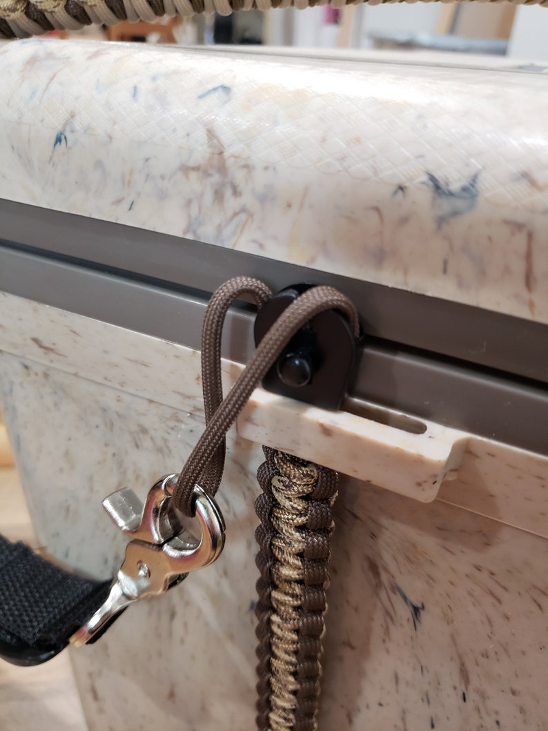 May include: Close-up of a cooler with a speckled white and brown exterior. A brown rope is attached to the cooler with a metal clasp and a braided strap. The cooler has a grey trim.