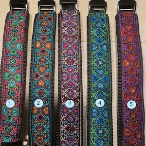 May include: Five fabric collars with black plastic side-release buckles, each featuring a distinct intricate woven pattern with embedded rhinestones. The collars are numbered one through five, displaying color variations of pink, teal, purple, and green.