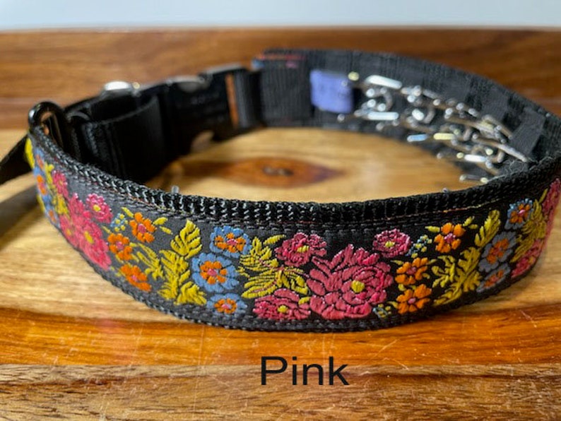 May include: A black nylon collar featuring a vibrant embroidered floral pattern in shades of pink, orange, yellow, and blue. The collar includes a black plastic side-release buckle, a metal D-ring, and a metal prong chain attachment. The text Pink is visible.