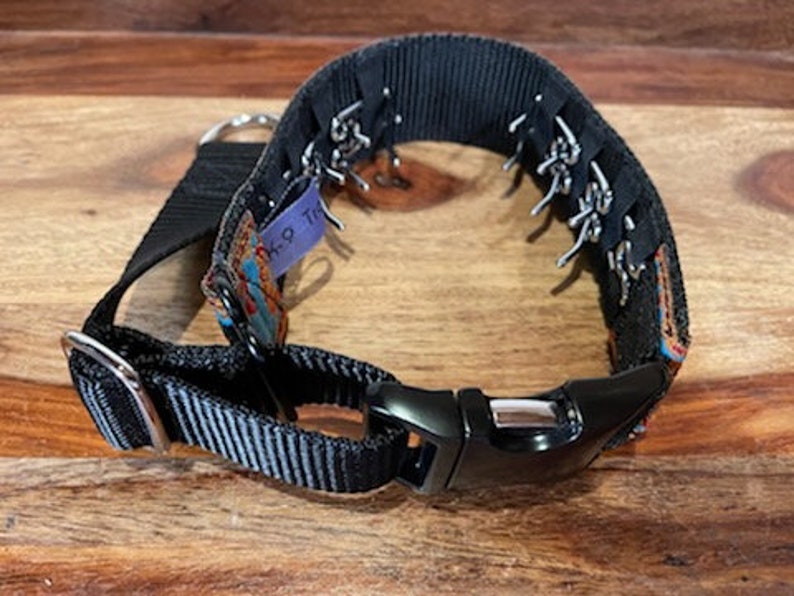 May include: Black dog collar with a silver buckle and a colourful patterned fabric insert. The collar has a series of silver loops on the side.