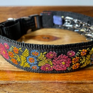 May include: A black nylon dog collar featuring a vibrant embroidered floral pattern in shades of pink, orange, yellow, and light blue. The collar includes a black plastic side-release buckle and a metal prong link chain section for adjustment.