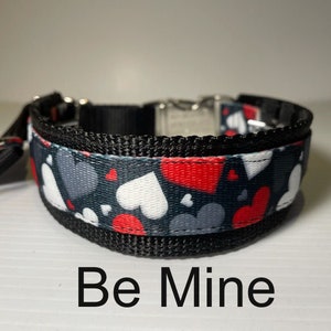 May include: Black and grey dog collar with a red, white and grey heart pattern. The collar has the text "Be Mine" printed below it.
