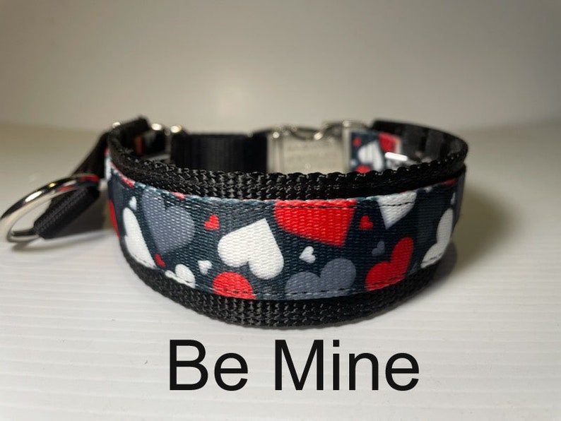 May include: Black and grey dog collar with a red, white and grey heart pattern. The collar has the text "Be Mine" printed below it.