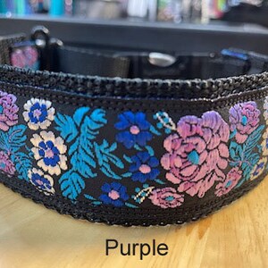 May include: A black pet collar featuring an embroidered floral pattern in shades of purple, light blue, and white. The collar includes a black plastic side-release buckle and a metal D-ring. The word Purple is printed below the collar.