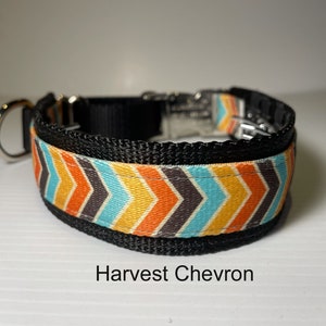 May include: A black dog collar with a colourful chevron pattern in orange, yellow, blue, and grey. The collar has a silver buckle and a D-ring. The text "Harvest Chevron" is printed below the collar.