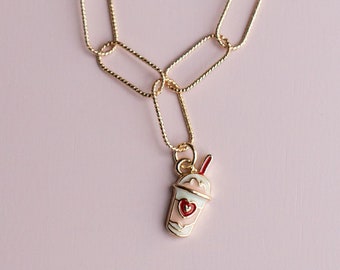 May include: A gold chain necklace with a charm of a pink milkshake with a red heart and a red straw. The chain is made of oval links.