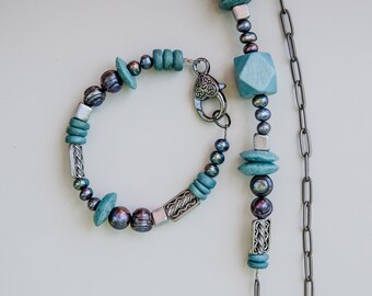 May include: A teal and silver necklace and bracelet set with dark grey pearls and wooden beads.
