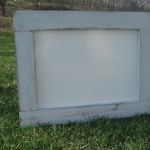 May include: A white framed sign with a distressed, light blue paint finish. The sign is made of wood and has a rectangular shape.