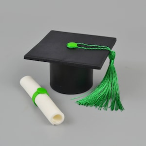 May include: A black graduation cap with a green tassel and a white scroll tied with a green ribbon.