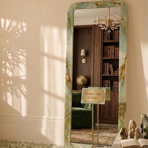 May include: A tall, rectangular floor mirror with rounded corners and a polished green onyx frame featuring natural brown veining. A small, rectangular sign on a gold metal stand in front of the mirror displays the text Stone Craft Gallery.