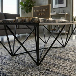 May include: A modern coffee table with a geometric black metal base and a stone top. The stone top has a mix of gray, white, and brown colors. The table is in a living room setting with a sign that reads "Stone Craft Gallery".