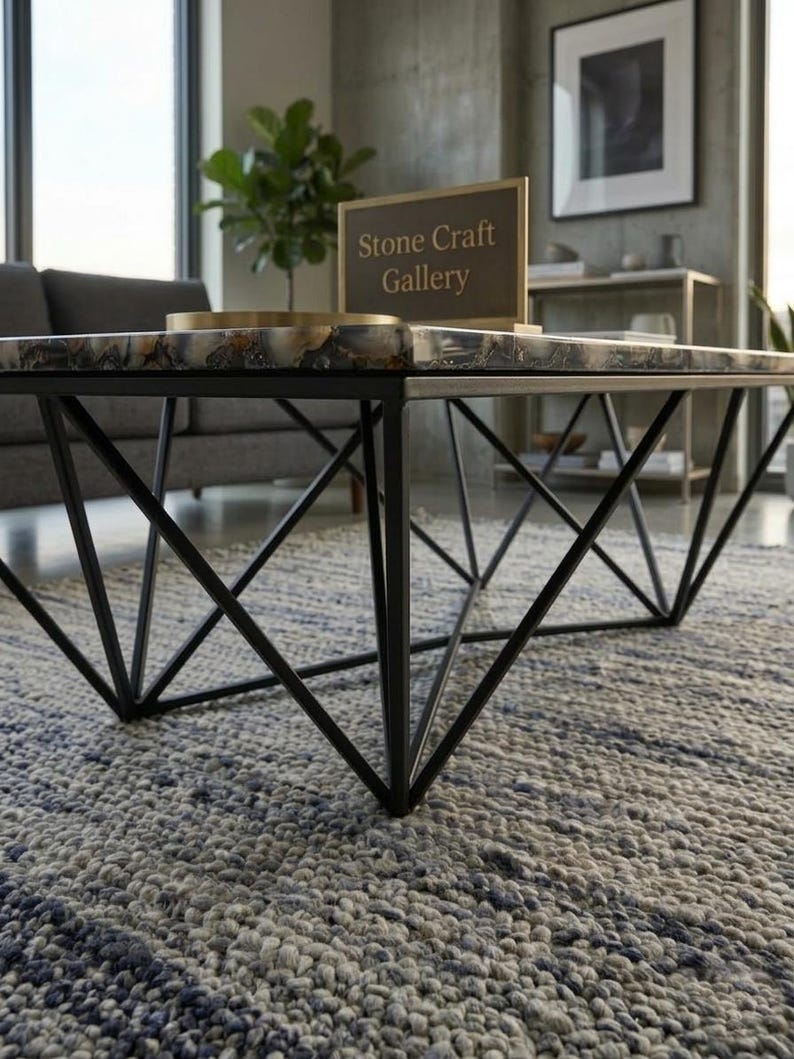 May include: A modern coffee table with a geometric black metal base and a stone top. The stone top has a mix of gray, white, and brown colors. The table is in a living room setting with a sign that reads "Stone Craft Gallery".