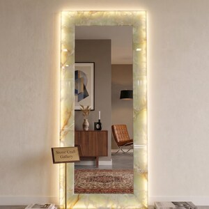 May include: A rectangular floor mirror featuring a translucent, backlit onyx stone frame with natural cream and amber veining. The mirror is illuminated by an integrated light source and includes a small sign reading Stone Craft Gallery.