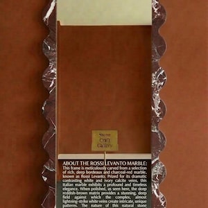 May include: A rectangular frame with a wavy edge, crafted from deep burgundy and charcoal-red marble. The frame has white and ivory veins, and a small sign that says "Stone Craft Gallery".