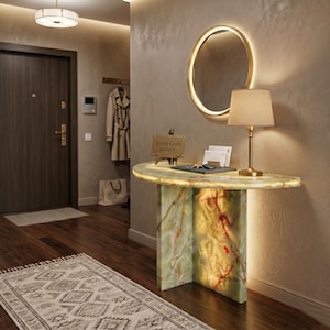 Può includere: Un ingresso con una consolle in marmo verde e bianco con piano luminoso. Uno specchio con cornice dorata e una lampada con paralume beige sono sulla parete. Il testo "Stone Craft Gallery" è su un piccolo cartello.