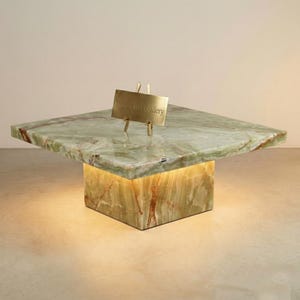 May include: A square, green onyx coffee table with a rectangular base. The table has a gold sign that reads "Stone Craft Gallery". The base of the table is illuminated with a warm light.