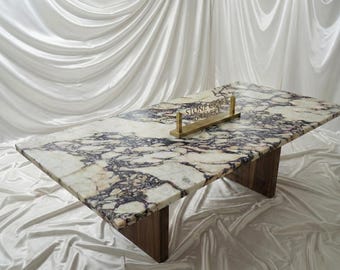 May include: A rectangular marble table with a white and purple patterned surface. The table has a wooden base and a gold sign that reads "STONE CRAFT GALLERY". The table is set against a white draped background.