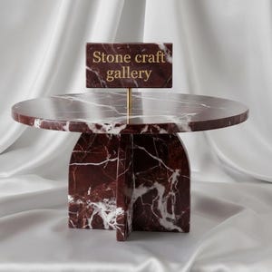 May include: A modern, marble-topped side table with a unique geometric base. The table is a deep burgundy color with white veining, and a sign that reads "Stone craft gallery" is displayed on top.