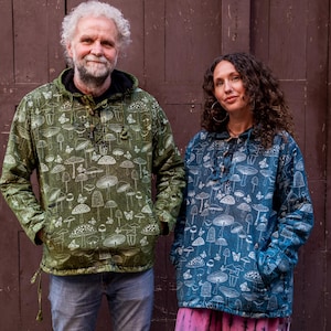 May include: Two people wearing green and blue patterned shirts with a mushroom design. The man is wearing jeans and the woman is wearing pink tie-dye trousers.