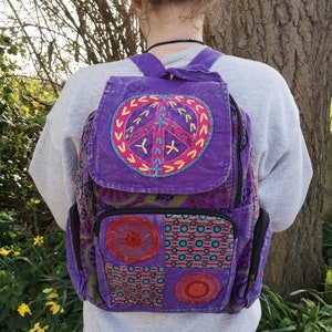 May include: Purple patchwork backpack with a large embroidered peace sign on the front. The backpack has a variety of colorful patterns and designs.