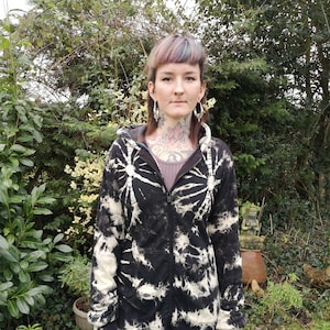 Peut inclure: Un sweat à capuche long en tie-dye noir et blanc avec une fermeture éclair. Le sweat-shirt a une coupe ample et une longueur longue.