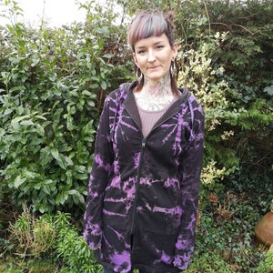 Könnte beinhalten: Ein langärmliger, tie-dye Hoodie in Schwarz und Lila mit Reißverschluss. Der Hoodie hat eine Kapuze und eine lockere Passform.