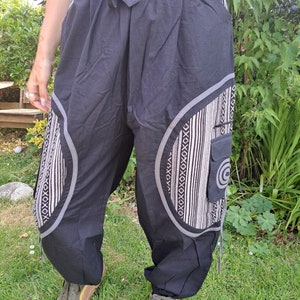 May include: Black pants with a white and gray geometric pattern on the legs. The pants have a drawstring waist and a side pocket.