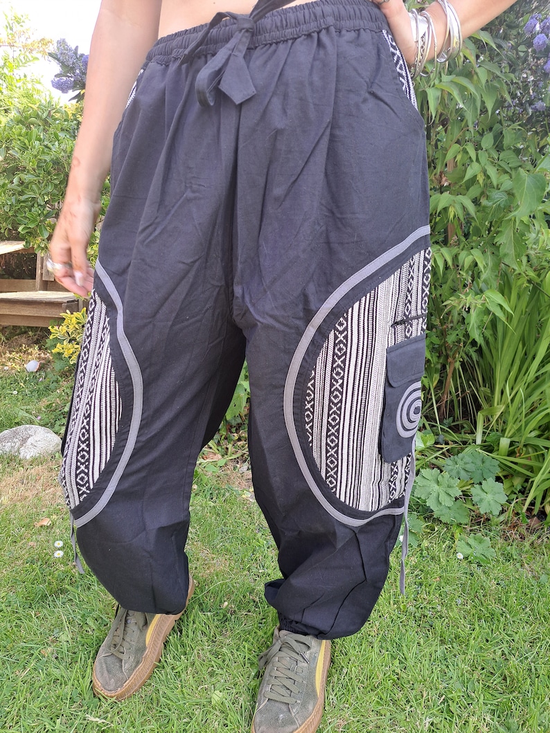 May include: Black pants with a white and gray geometric pattern on the legs. The pants have a drawstring waist and a side pocket.