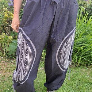 May include: Black pants with a white geometric pattern on the sides. The pants have a drawstring waistband and a relaxed fit.
