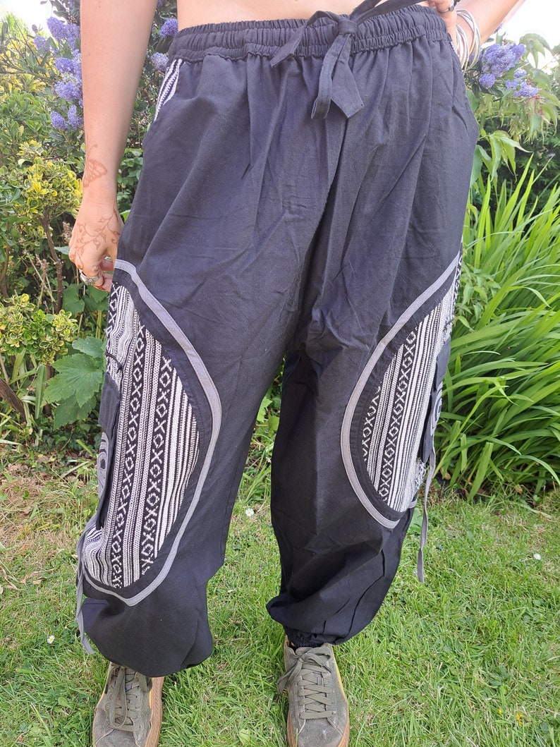 May include: Black pants with a white geometric pattern on the sides. The pants have a drawstring waistband and a relaxed fit.