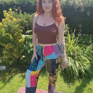 May include: A woman wearing a brown tank top and colorful patchwork pants. The pants have a tie waist and are made of different fabrics and patterns.