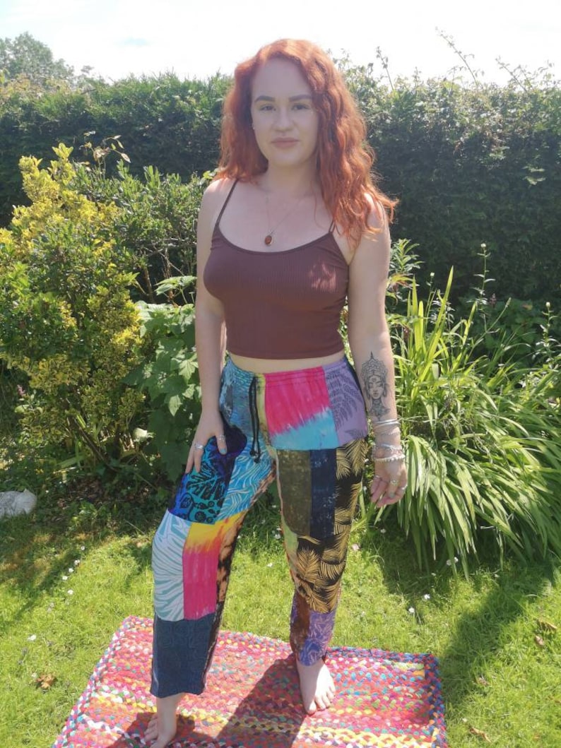 May include: A woman wearing a brown tank top and colorful patchwork pants. The pants have a tie waist and are made of different fabrics and patterns.