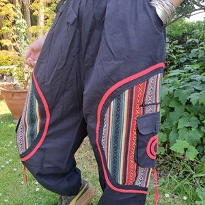 May include: Black pants with red trim and colorful patterned fabric accents. The pants have a drawstring waist and a cargo pocket.