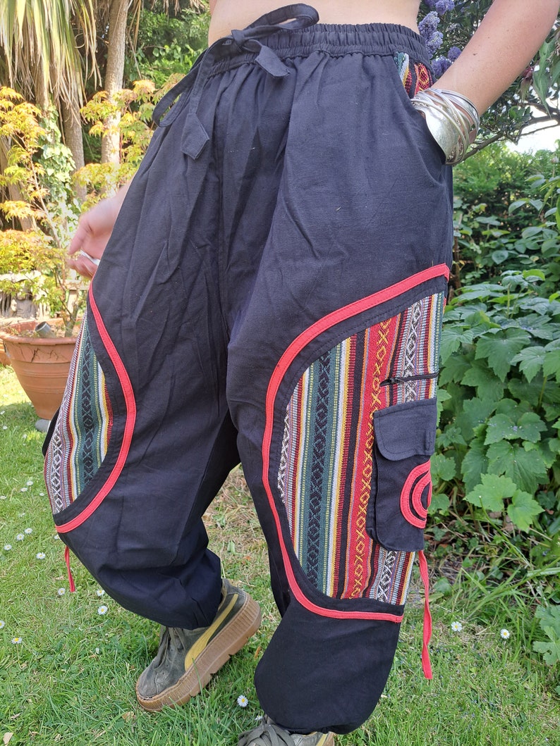 May include: Black pants with red trim and colorful patterned fabric accents. The pants have a drawstring waist and a cargo pocket.